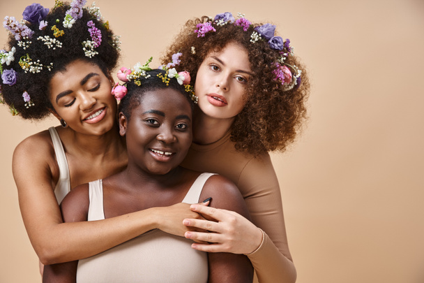 γοητευτικό πολυφυλετικές γυναίκες σε εσώρουχα με πολύχρωμα λουλούδια στα μαλλιά σε μπεζ, συν το μέγεθος ομορφιά - Φωτογραφία, εικόνα
