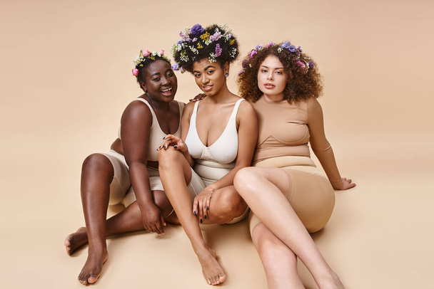 diverse multiethnic girlfriends in lingerie with flowers in hair sitting on beige, plus size beauty - Foto, imagen