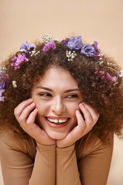 retrato de mujer bonita y alegre con flores de colores en el pelo ondulado en beige, belleza natural - Foto, imagen