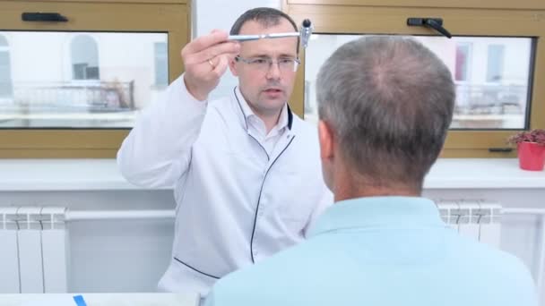 een mannelijke neuroloog rijdt een hamer voor de ogen van de patiënt tijdens een routine onderzoek in de kliniek - Video
