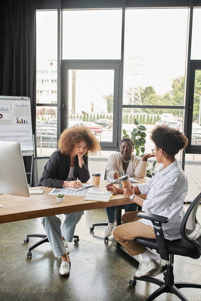 multikulturális üzletasszonyok sokszínű csoportja, akik a laptop és az irodai dokumentumok közelében lévő startup-ról beszélgetnek - Fotó, kép
