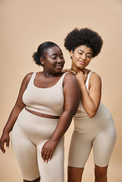 cheerful african american female models in underwear posing on beige, natural plus size beauty - Photo, Image