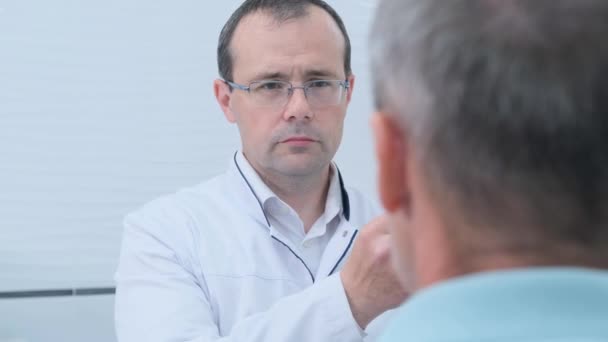 een mannelijke neuroloog rijdt een hamer voor de ogen van de patiënt tijdens een routine onderzoek in de kliniek - Video