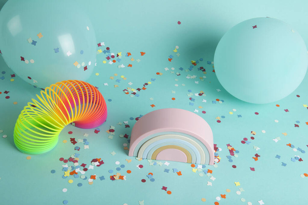  a plastic rainbow toy and a slinky in front of balloons of the same color as the background and confetti on the ground. The composition is in turquoise-green color palette.  - Photo, Image