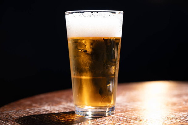 Pintová sklenice studeného čerstvého britského piva a ležáckého piva podávaná ve staré staroanglické hospodě, tmavé pozadí - Fotografie, Obrázek