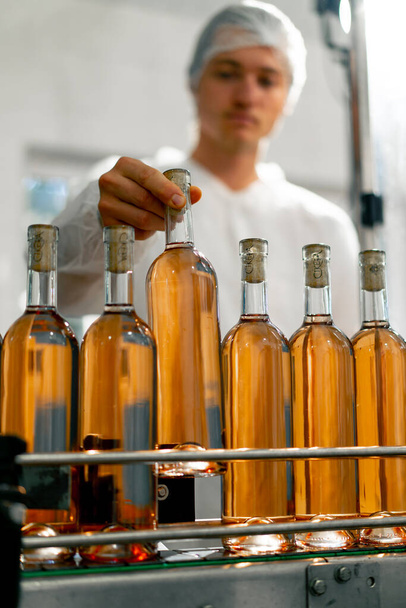 Um tecnólogo masculino controla o processo de embalagem e distribuição de garrafas de vinho na produção - Foto, Imagem