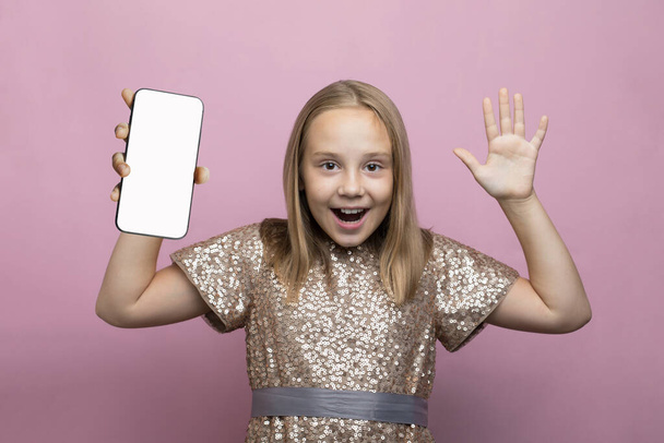 Lindo niño sorprendido sosteniendo teléfono inteligente con pantalla blanca vacía en blanco para la nueva aplicación o sitio web móvil sobre fondo rosa - Foto, imagen