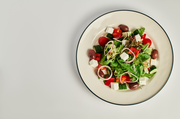 foto vista superior del plato con ensalada griega tradicional recién hecha sobre fondo gris, alimentación saludable - Foto, Imagen