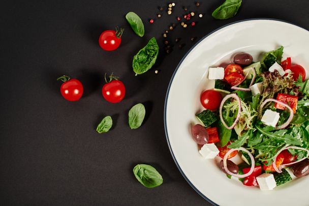 vue du dessus photo de l'assiette avec salade grecque traditionnelle près de tomates cerises sur fond noir - Photo, image
