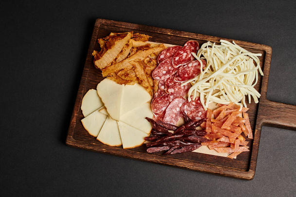 вид зверху на дошку з гарбузовим вибором сиру, сушеною яловичиною та скибочками салямі на чорному - Фото, зображення