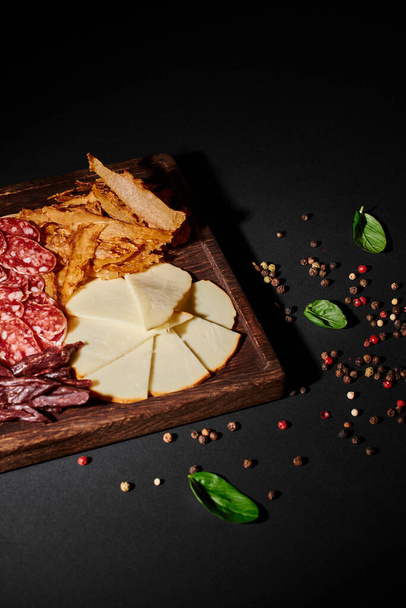 planche de charcuterie savoureuse avec sélection de fromages gastronomiques, boeuf séché et salami sur noir - Photo, image