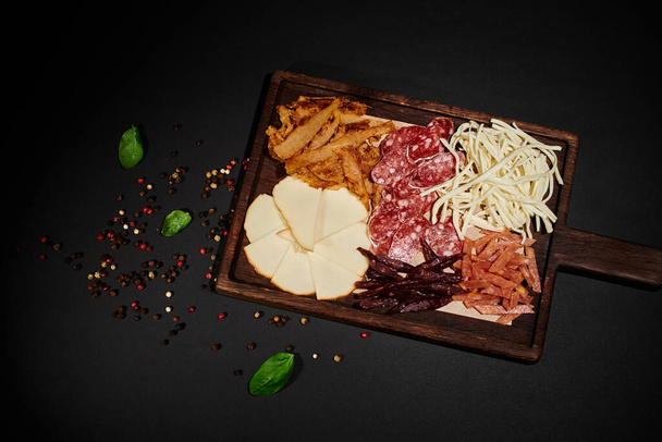 felső kilátás party élelmiszer-ellátás ínyenc sajt kiválasztása, szárított marhahús és szalámi szeletek fekete - Fotó, kép