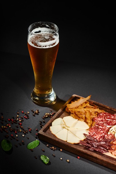Ποτήρι μπύρας craft κοντά στο charcuterie board με γκουρμέ τυρί, αποξηραμένο βοδινό και σαλάμι επί του σκάφους - Φωτογραφία, εικόνα