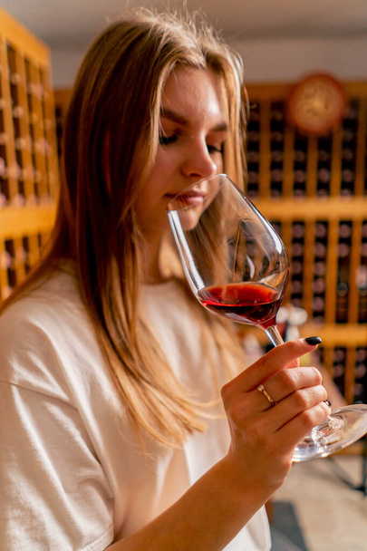 Foto ravvicinata di una ragazza che assaggia vino invecchiato, lo porta al naso e inala l'aroma della bevanda - Foto, immagini
