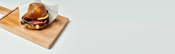 ζουμερό χάμπουργκερ με ψητό μοσχάρι, κόκκινο κρεμμύδι, λιωμένο τυρί και κουλούρι σουσάμι σε ξύλινη σανίδα, λάβαρο - Φωτογραφία, εικόνα