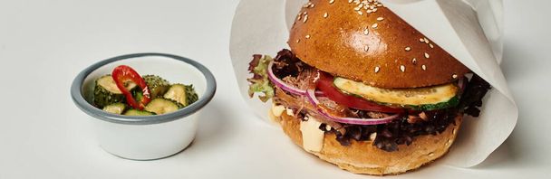 Hamburger pankartı, susamlı ekmek, biftek ve turşu, ahşap tepside, gri arka planda. - Fotoğraf, Görsel