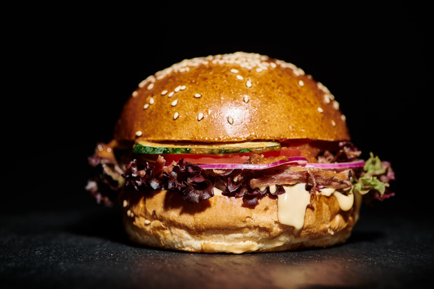 juicy hamburger with bacon, red onion, cheese melt and sesame bun on black background, close up - Photo, Image