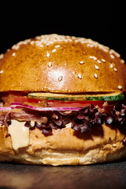 tasty hamburger with bacon, red onion, cheese melt and sesame bun on black background, close up - Photo, Image