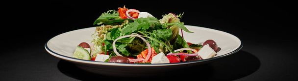 πανό υγιεινής διατροφής, νόστιμη ελληνική σαλάτα με φέτα, κόκκινο κρεμμύδι, φύλλα ρόκα σε μαύρο - Φωτογραφία, εικόνα