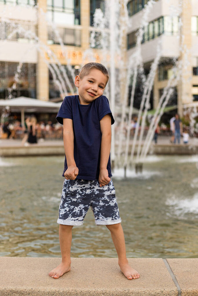 Un ragazzo allegro sta vicino alla fontana. Buona infanzia. Genitori, libertà. Foto di alta qualità - Foto, immagini