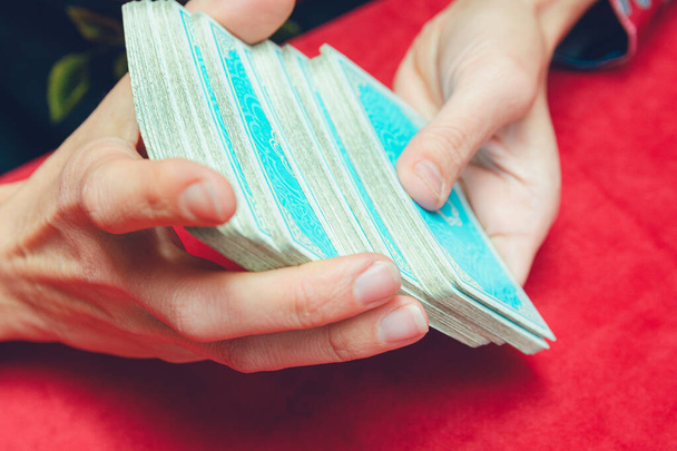 Крупним планом руки невпізнаваного молодого кавказького читача таро Жінка змішуючи сині картки таро на столі з червоною скатертиною. - Фото, зображення