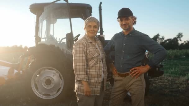 Çiftlik arazisinde gün ışığında duran neşeli adam ve kadın. İki çiftçi traktör arka planında gülümsüyor. Yaz ekimi mevsimi. Hasat mevsimi. Tarım ve saban.. - Video, Çekim