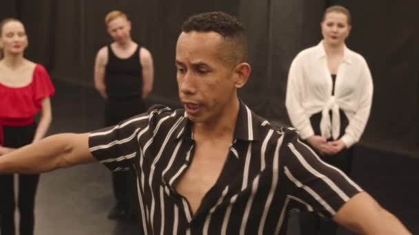Ralentissement moyen de l'enseignant hispanique de danse masculine montrant des mouvements de danse latine à un groupe de personnes assistant à sa classe de maître en studio - Séquence, vidéo