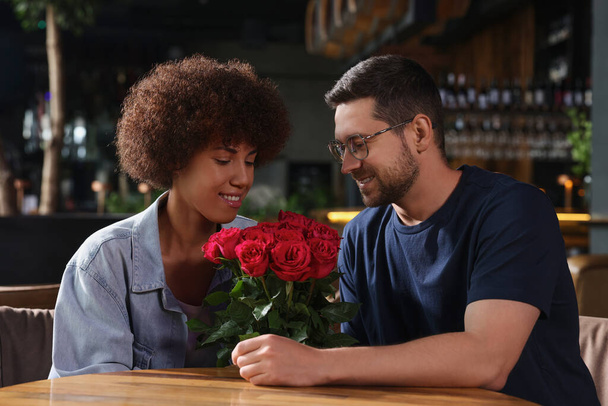 International relationships. Handsome man presenting roses to his beloved woman in cafe - Zdjęcie, obraz