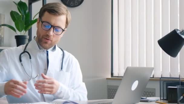 Αρσενικό γιατρό gesturing ενώ μιλάμε για βιντεοκλήση μέσω ψηφιακής ταμπλέτας στο γραφείο γιατρούς. Τηλεϊατρική έννοια μακρινή υγειονομική περίθαλψη. - Πλάνα, βίντεο