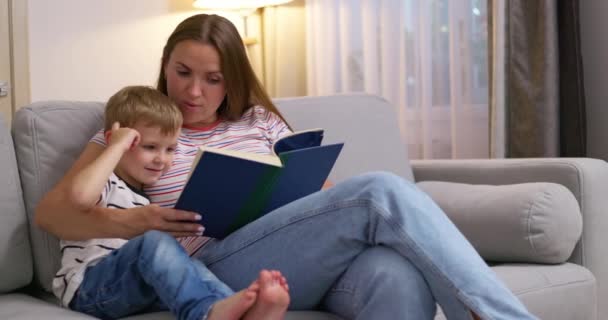 Mutter und Sohn lesen ein Buch, sitzen auf einem gemütlichen Sofa im Wohnzimmer, Familienzeit. Hochwertiges 4k Filmmaterial - Filmmaterial, Video