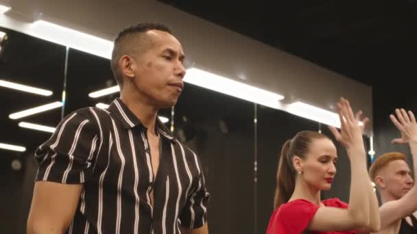Slowmo de charismatique jeune homme hispanique en chemise à rayures v cou danse Latina avec un groupe d'étudiants dans un studio de danse spacieux - Séquence, vidéo