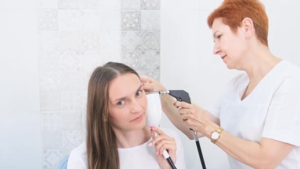 Otolaryngologi suorittaa earwash ja earwax poisto nuori aikuinen nainen käyttää nykyaikaisia lääketieteellisiä laitteita. Terveydenhuollon ja lääketieteen käsite. - Materiaali, video
