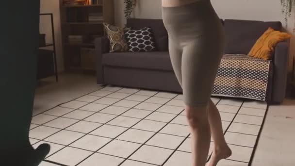 Gehakt shot van onherkenbare jonge actieve vrouw in strakke sportkleding uitrollen yoga mat op de vloer in de woonkamer tijdens de training thuis - Video