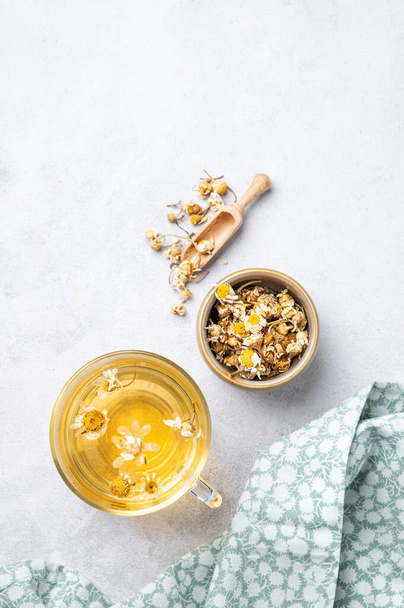 Chamomile herbal tea in a glass cup on a light background with dry flowers and napkin. The concept of a healthy detox drink for health and sleep. Top view and copy space.  - Photo, Image