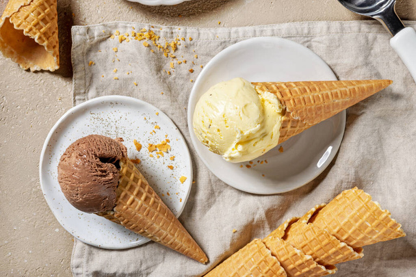 glace au chocolat et à la vanille dans des cônes de gaufres sur des assiettes, vue de dessus - Photo, image