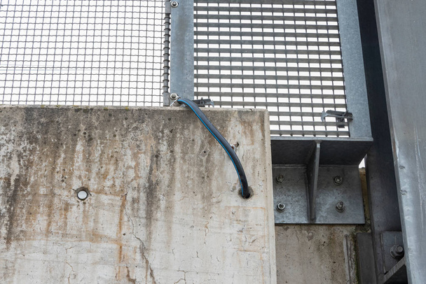 Металлический контакт земного электрода. Железный забор моста заземляется на бетонный тротуар с помощью кабеля. - Фото, изображение