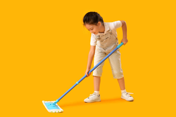 Cute little girl with mop on yellow background - Photo, Image