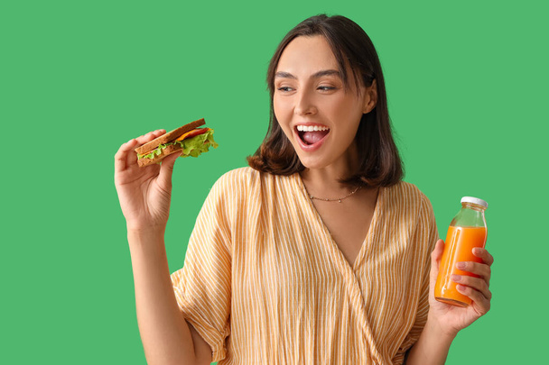 Gyönyörű fiatal nő ízletes szendvics és narancslé zöld háttér - Fotó, kép
