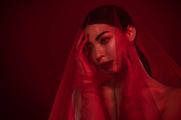 Фото азиатской девушки роковой прикосновение лица кружева вуаль платье плечи от изолированных темно-красный цвет фона. - Фото, изображение