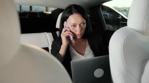 Ocupada mujer de negocios hablando por teléfono móvil y escribiendo en el portátil durante el viaje en el coche. Transporte, tecnología, viaje, concepto de negocio. Movimiento lento - Metraje, vídeo