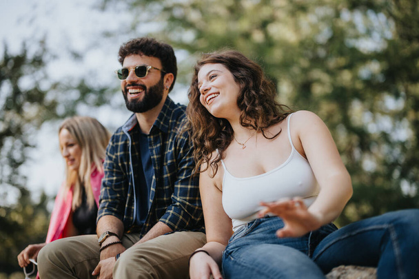 Friends chat and relax in the park, surrounded by nature. Their joyful energy is uplifting and carefree. A perfect moment of leisure, enjoying positive vibes and a sunny day. - Photo, Image