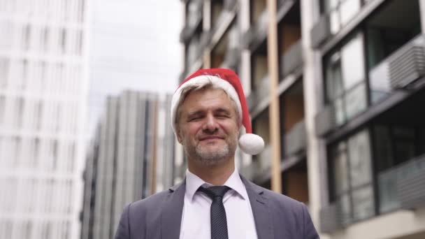 Hymyilevä liikemies Santa hattu samalla pyörii ympäriinsä, kun seisoo vastaan business center. Juhla, joulu, loma, liikeidea. Hidastus - Materiaali, video