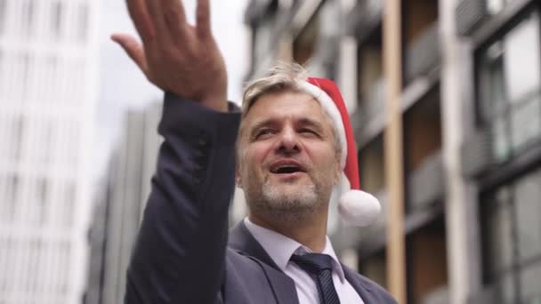 Hymyilevä tyylikäs aikuinen liikemies kiinni lumihiutale kädestä seistessään ulkona, yllään Santa hattu. Juhla, joulu, loma, liikeidea. Hidastus - Materiaali, video