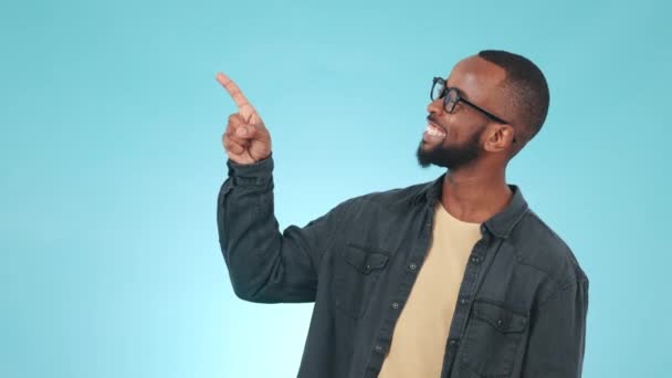 Pointing, mockup and face of black man in a studio to empty space for sign or advertising. Happy, smile and portrait of African male model with an ok hand gesture isolated by blue background - Footage, Video