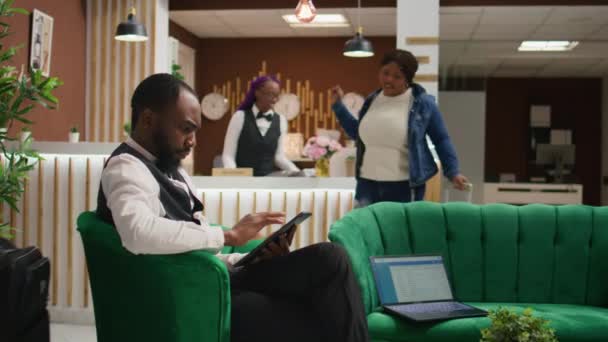 Afrikalı Amerikalı personel lobideki tablette online rezervasyon yapıyor, lüks bir otelde çalışıyor ve misafirler için mükemmel bir kapıcı hizmeti sunuyor. Bellboy üniformalı, odaları yönetiyor.. - Video, Çekim