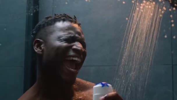 Uomo afroamericano che canta in bagno divertendosi spensierato felice etnico muscolare atletica maschile energia ballando alla musica cantare con bottiglia shampoo gel doccia rinfrescare il corpo mattina igiene balneare - Filmati, video