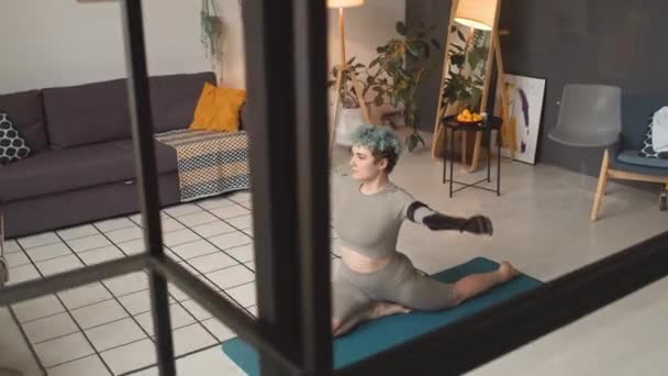 Fille caucasienne avec prothèse bras étirant sur tapis de yoga avec ses mains vers le haut faire la pratique de la respiration dans une atmosphère domestique confortable - Séquence, vidéo