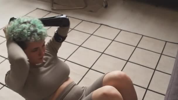 Van boven schot van vastberaden blanke meisje met kunstmatige arm doet crunches op de vloer in haar appartement tijdens huishoudelijke abs workout - Video