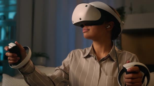 Femme afro-américaine jouer jeu de réalité virtuelle à la maison nuit divertissement fille ethnique dans VR casque et lunettes de dispositif moderne jouer avec des contrôleurs de jeu explorer le cyberespace 3D monde métaverse - Séquence, vidéo