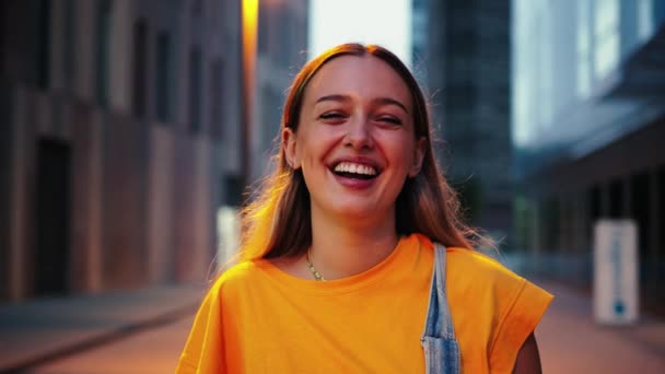 Індивідуальний портрет щасливої молодої кавказької жінки, що стоїть на вулиці, насолоджуючись нічним життям. Радісна дівчина-підліток в повсякденному одязі сміється, дивлячись на камеру з впевненою посмішкою на вулиці - Кадри, відео